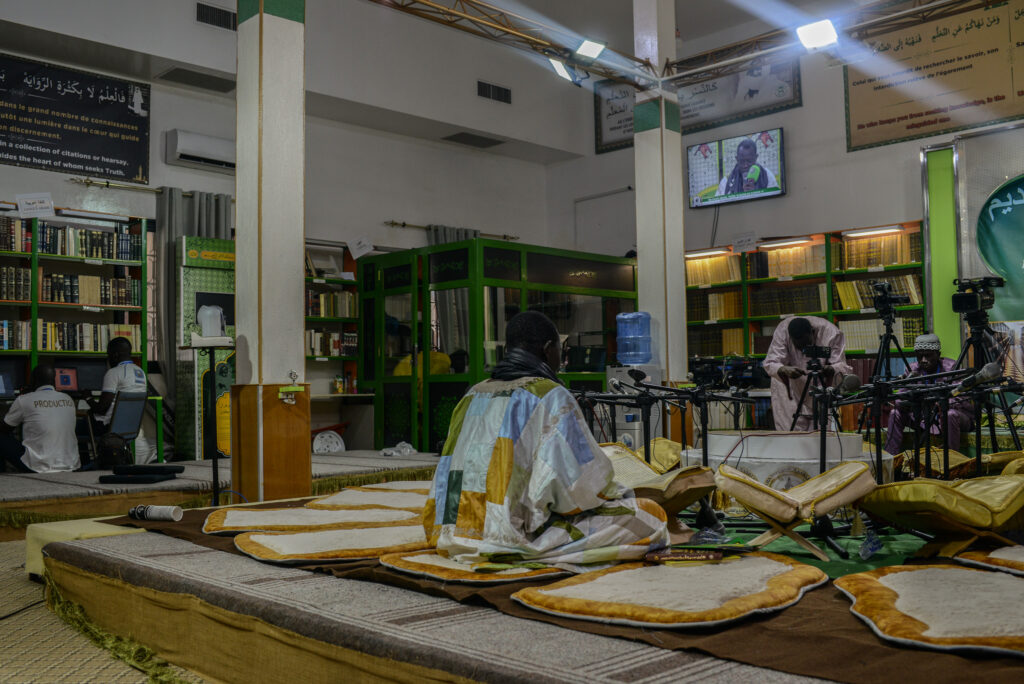 Pour répondre aux défis du 21e siècle, les mourides ont créé leur propre chaine de télévision retransmise via les plateforme telle que Youtube. Ici, une lecture d'un passage du Coran dans le batiment du Daaray Kamil. © Olivier Ceccaldi